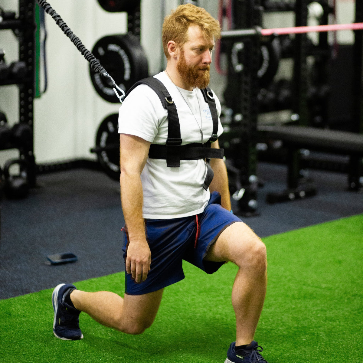 Man doing a lunge in the PUSH Perfect vest with the cord clipped to a gym rack