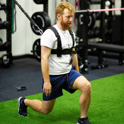 Man doing a lunge in the PUSH Perfect vest with the cord clipped to a gym rack