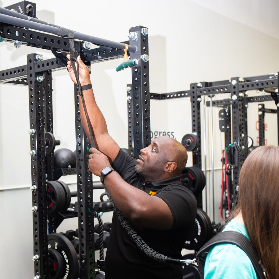 Trainer clipping the PUSH Perfect cord to a gym rack while a client wears the vest